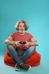 Photo of Emotional mature man playing video games with controller on color background. Space for text