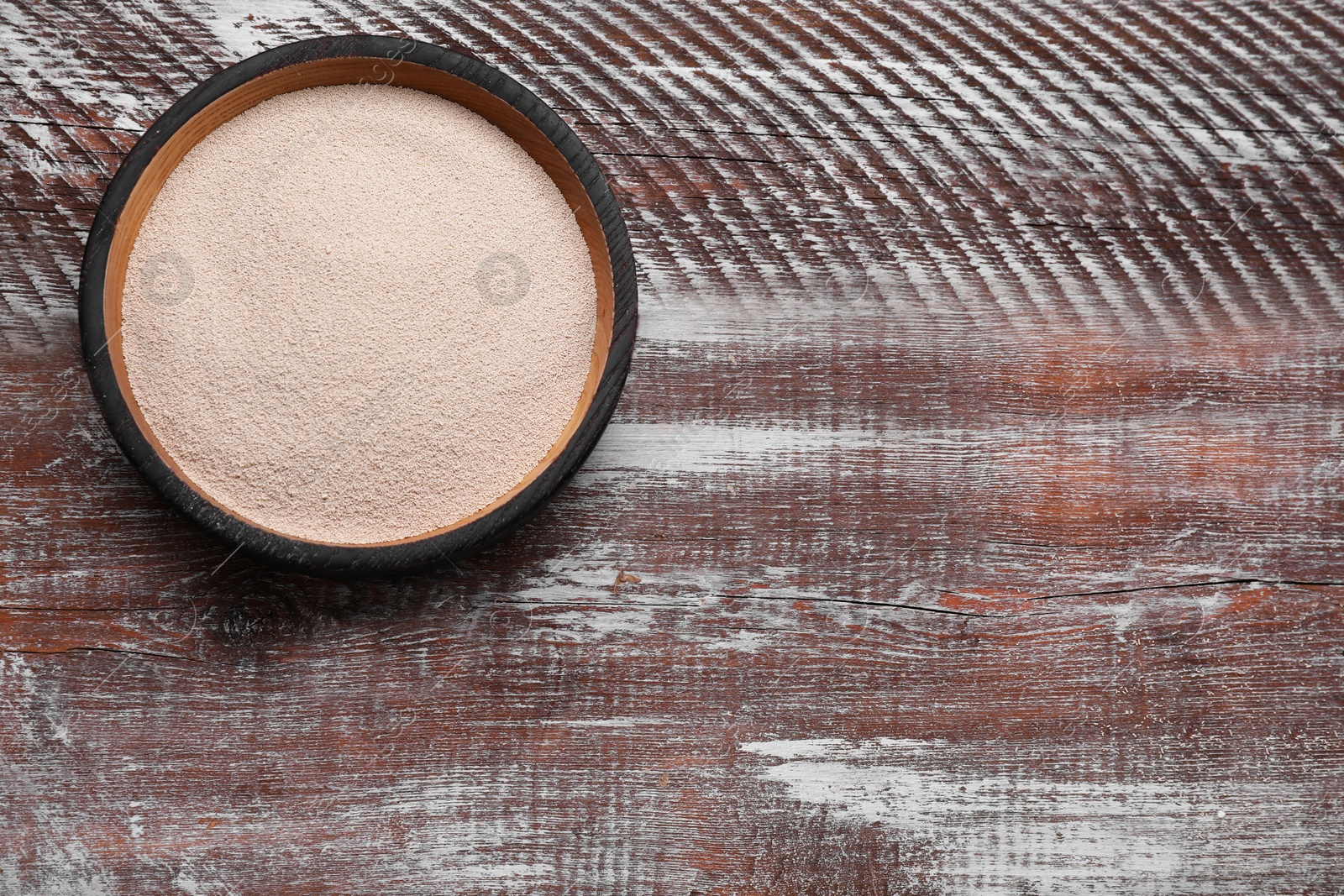 Photo of Bowl of active dry yeast on wooden table, top view. Space for text