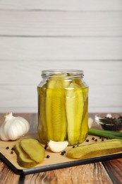 Jar with tasty pickled cucumbers and ingredients on wooden table