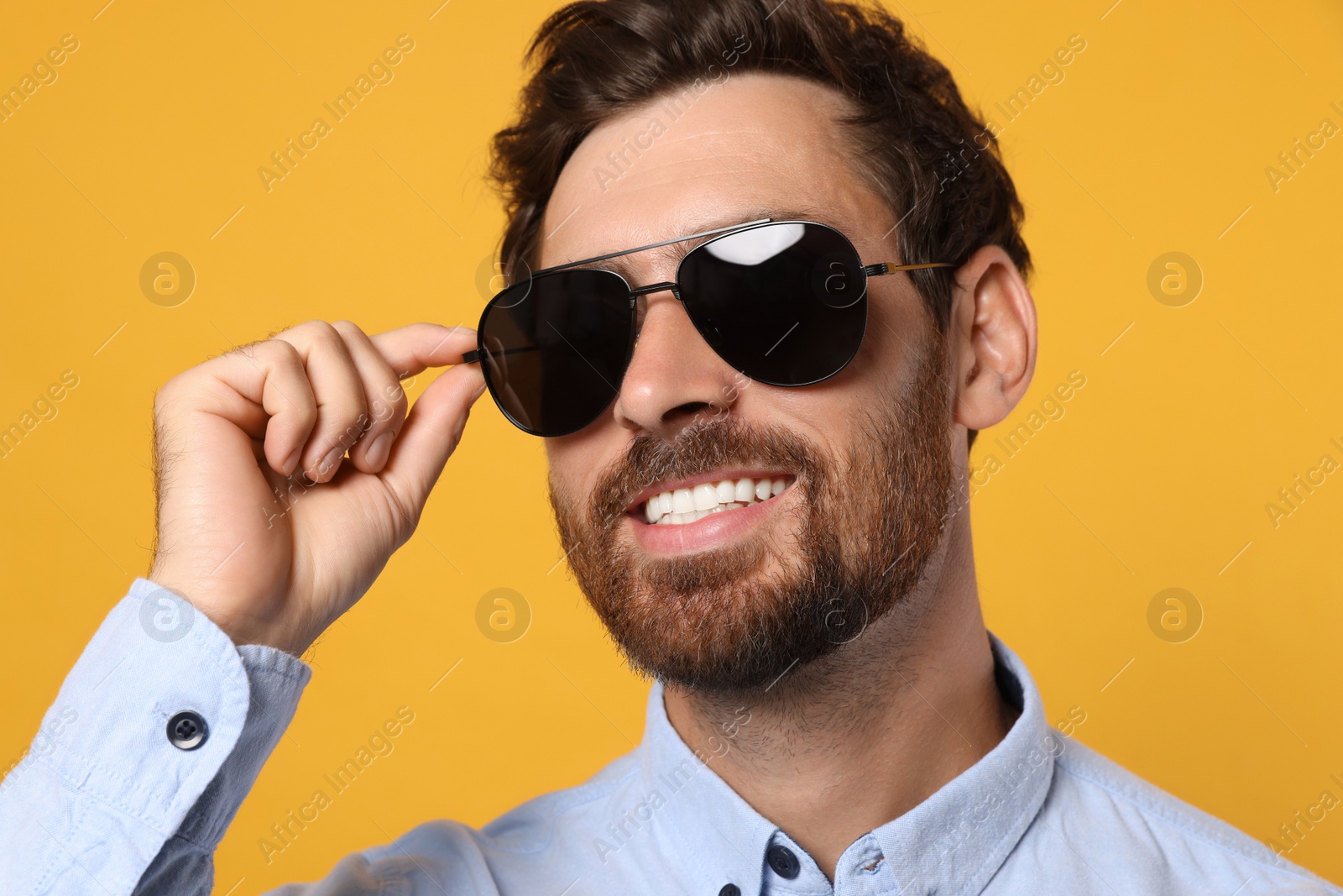 Photo of Portrait of smiling bearded man with stylish sunglasses on orange background, closeup
