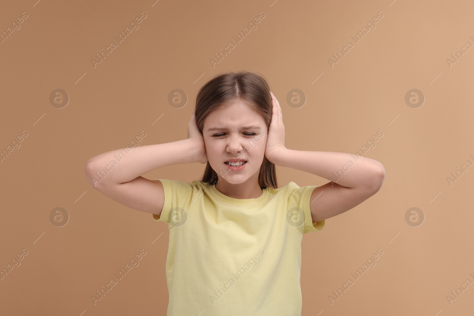 Photo of Hearing problem. Little girl suffering from ear pain on pale brown background