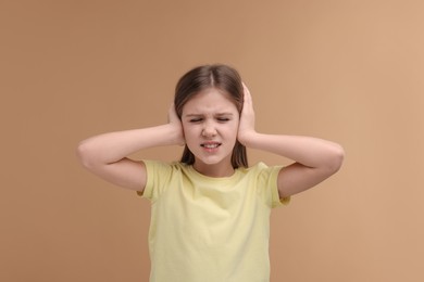Hearing problem. Little girl suffering from ear pain on pale brown background