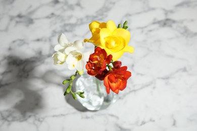 Photo of Bouquet of spring freesia flowers in vase on marble background, view from above