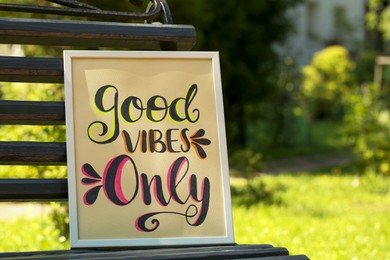 Photo of Poster with phrase Good Vibes Only on black wooden bench outdoors