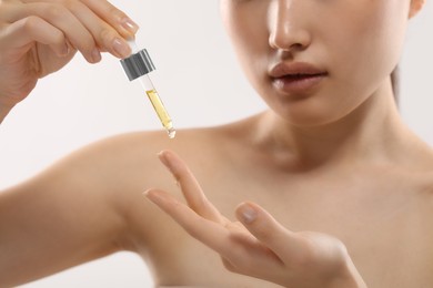 Photo of Beautiful young woman applying cosmetic serum onto her finger on white background, selective focus