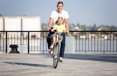 Father and daughter riding bicycle outdoors on sunny day