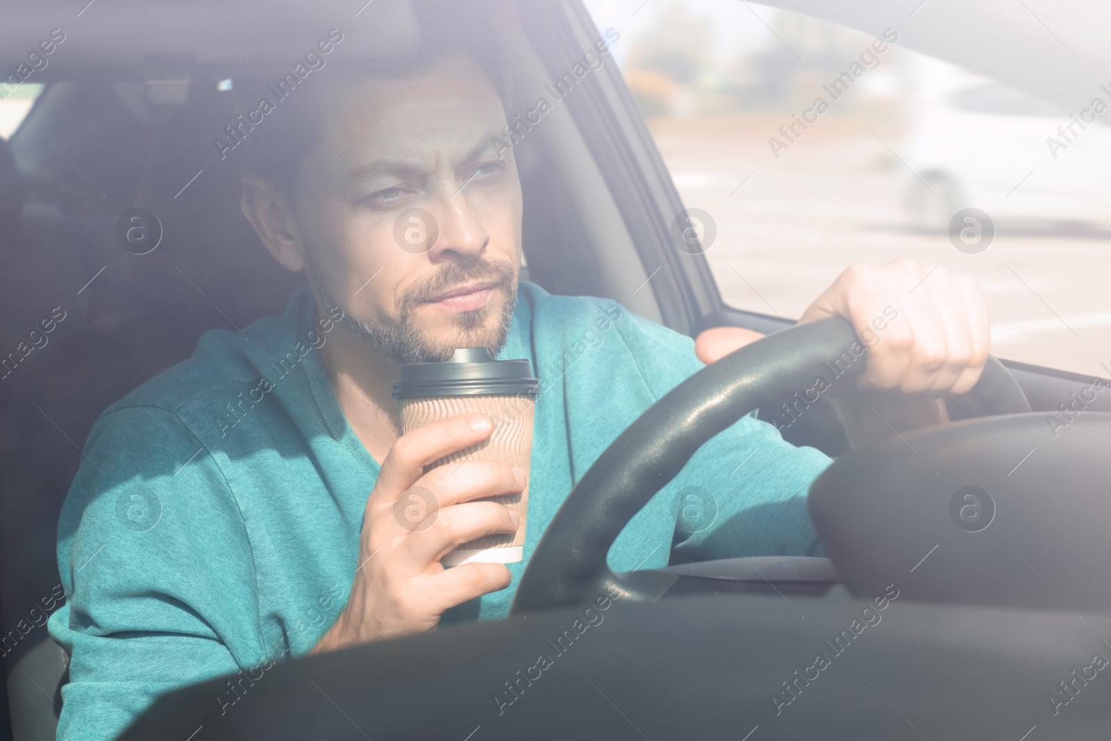 Photo of Sleepy tired man holding takeaway paper cup in his modern car, view from outside