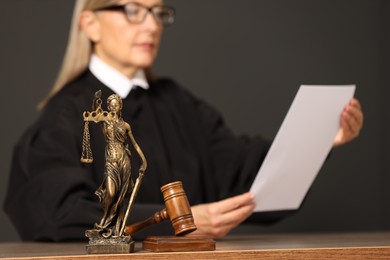 Photo of Judge working with document indoors, selective focus. Mallet and figure of Lady Justice on wooden table