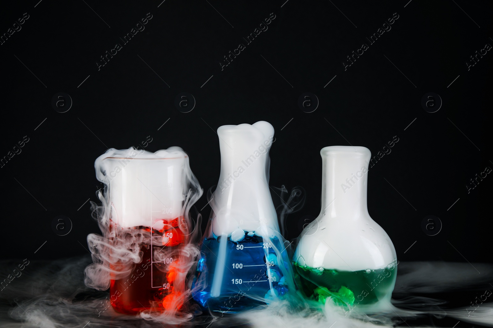 Photo of Laboratory glassware with colorful liquids and steam on black background. Chemical reaction