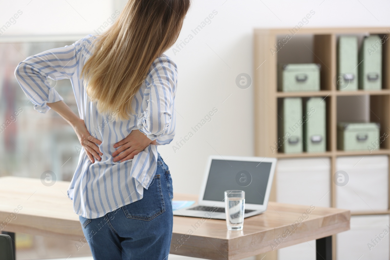 Photo of Woman suffering from back pain in office. Symptom of bad posture