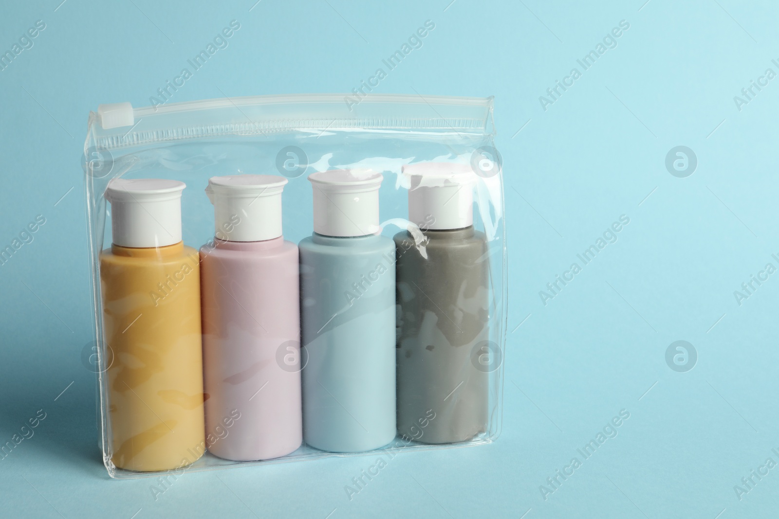 Photo of Cosmetic travel kit in plastic bag on light blue background. Space for text