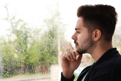Photo of Thoughtful handsome man near window indoors on rainy day