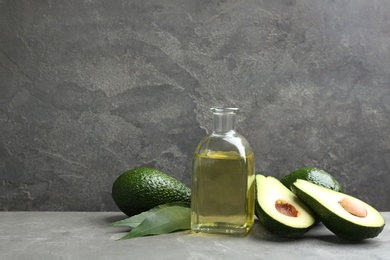 Photo of Bottle of natural oil and avocados on table against grey stone background. Space for text