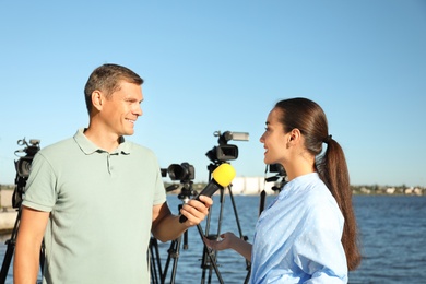 Photo of Professional journalist interviewing young woman near river on sunny day