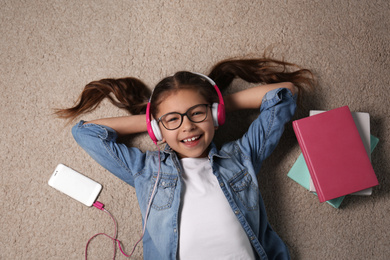 Photo of Cute little girl listening to audiobook on floor, top view