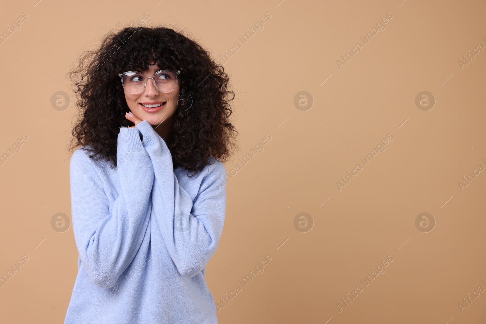 Photo of Happy young woman in stylish light blue sweater and glasses on beige background, space for text