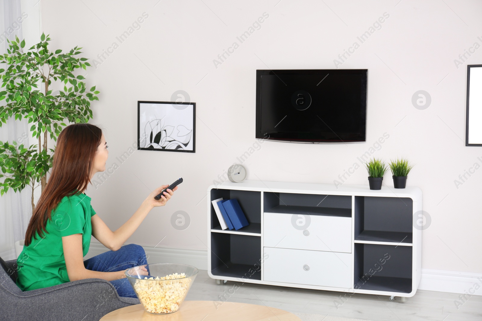 Photo of Young woman watching TV in armchair at home