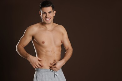 Photo of Fit man with marks on body against dark brown background, space for text. Weight loss surgery