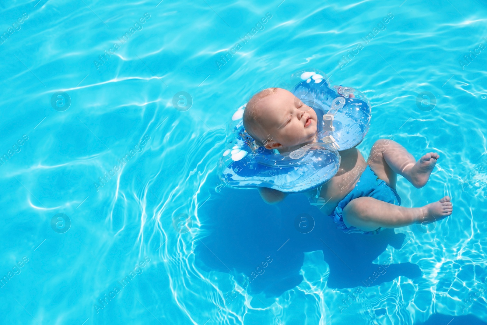 Photo of Cute little baby with inflatable neck ring in swimming pool on sunny day, outdoors