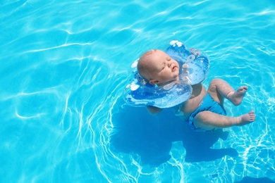 Photo of Cute little baby with inflatable neck ring in swimming pool on sunny day, outdoors