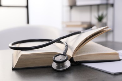 Open student textbook and stethoscope on grey table indoors, closeup. Medical education