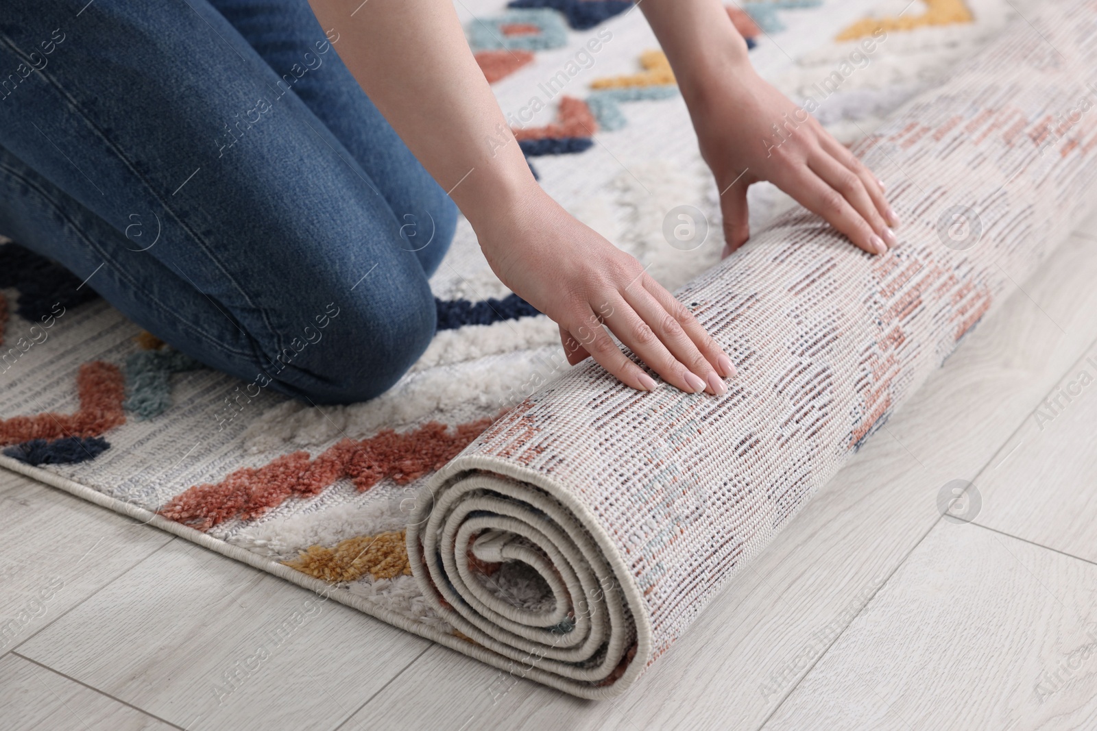 Photo of Woman unrolling carpet with beautiful pattern on floor in room, closeup