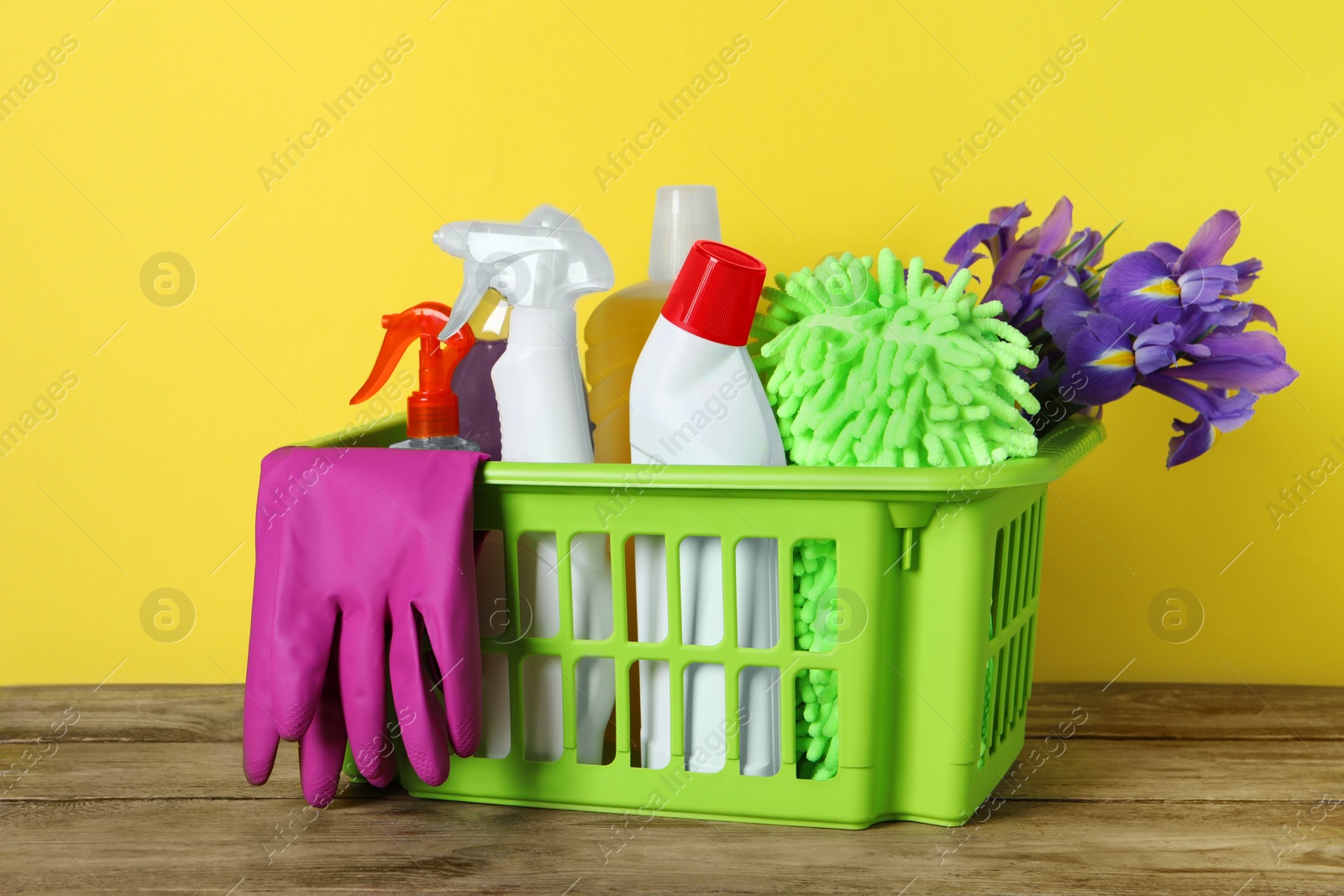 Photo of Spring cleaning. Basket with detergents, flowers and tools on wooden table