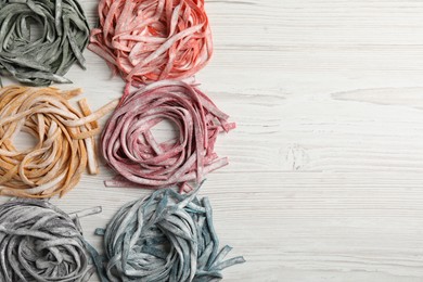Photo of Rolled pasta painted with different food colorings on white wooden table, flat lay. Space for text