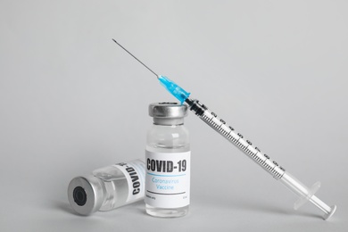 Vials with coronavirus vaccine and syringe on light background