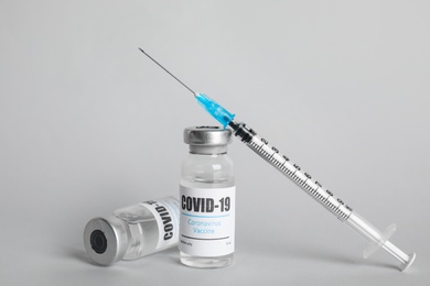 Photo of Vials with coronavirus vaccine and syringe on light background