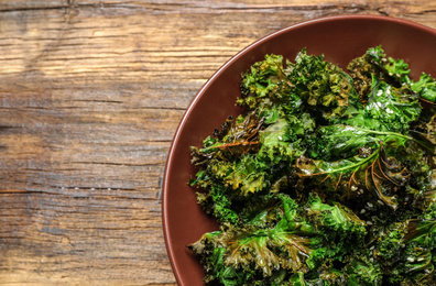 Photo of Tasty baked kale chips on wooden table, top view. Space for text