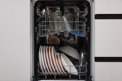 Photo of Open modern dishwasher with dirty tableware in kitchen