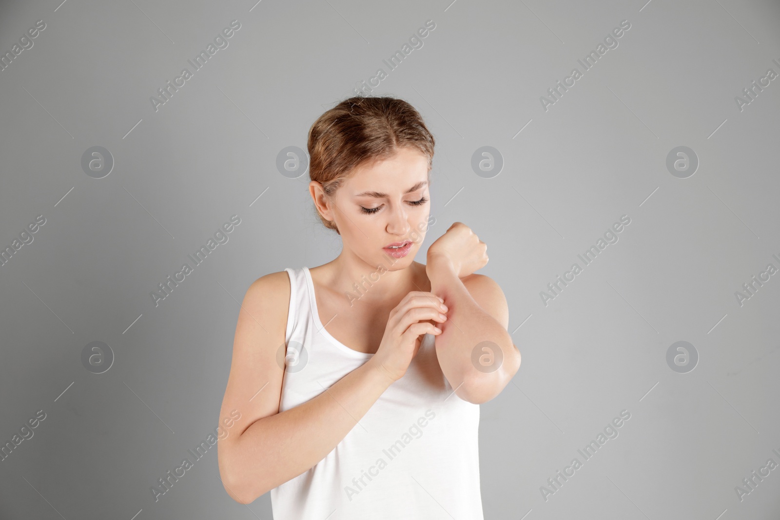 Photo of Woman scratching forearm on grey background. Allergy symptoms