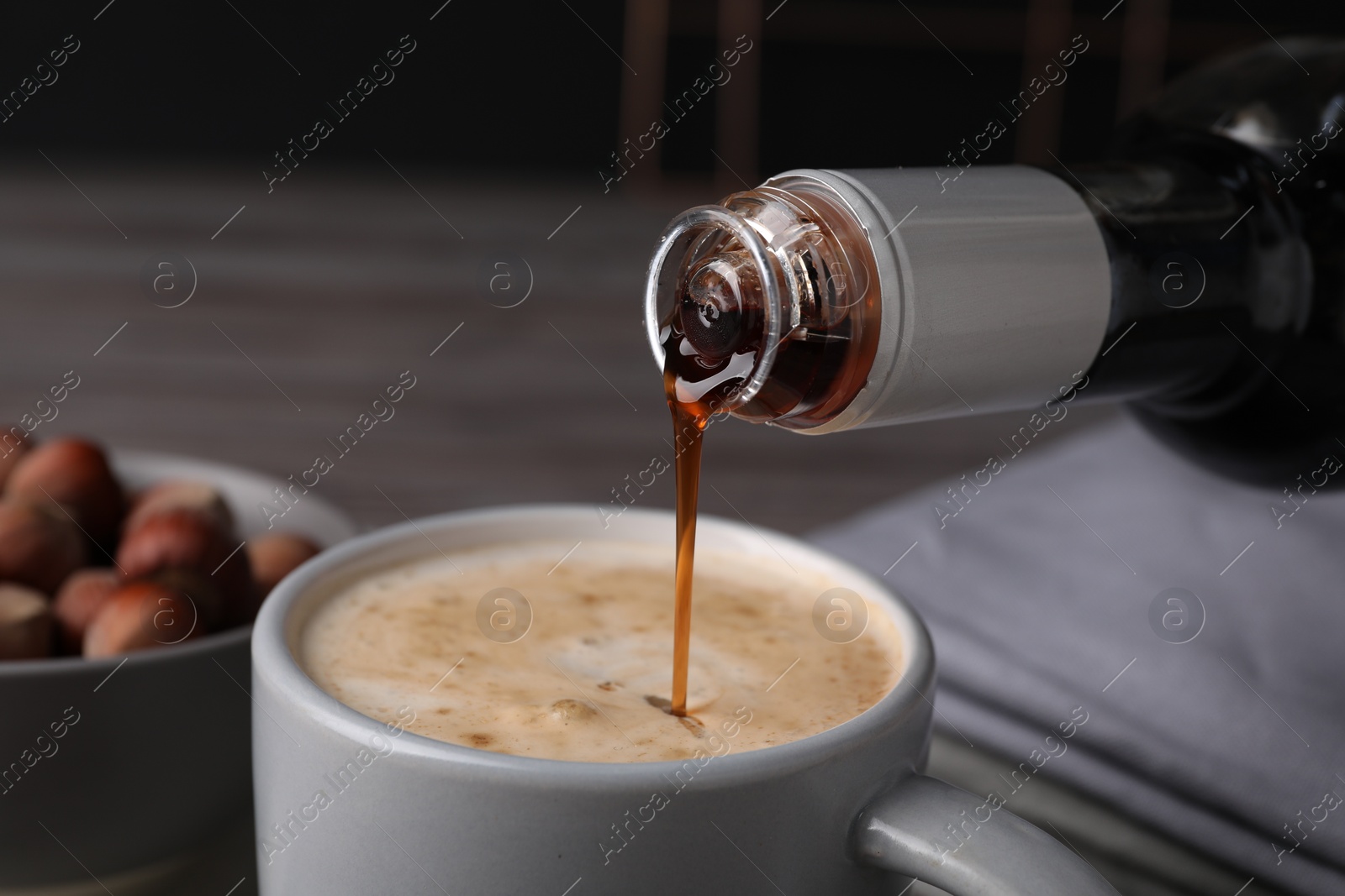 Photo of Pouring delicious hazelnut syrup into cup with coffee at table, closeup