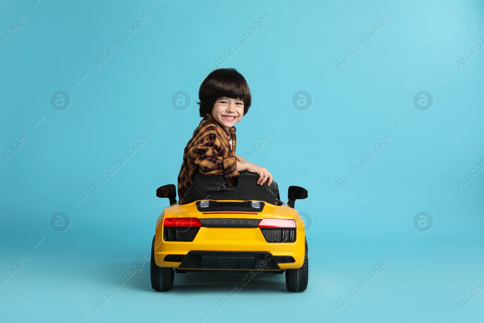 Photo of Little child driving yellow toy car on light blue background