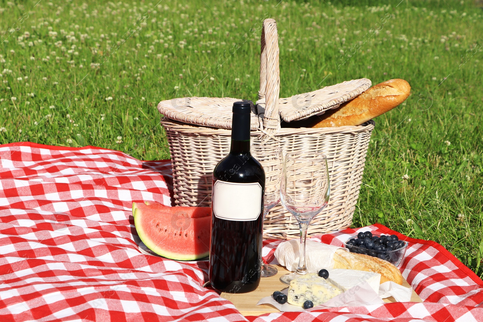 Photo of Picnic blanket with delicious food and wine outdoors on summer day