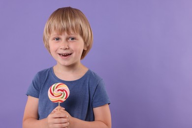 Happy little boy with colorful lollipop swirl on violet background, space for text