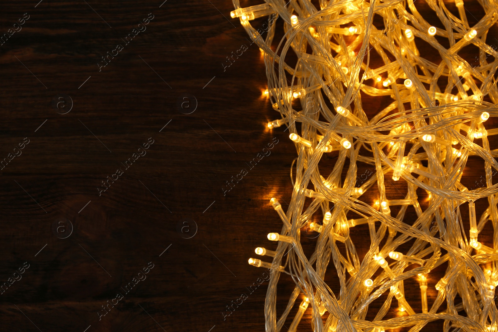 Photo of Glowing Christmas lights on wooden background, top view. Space for text