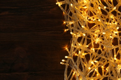 Photo of Glowing Christmas lights on wooden background, top view. Space for text