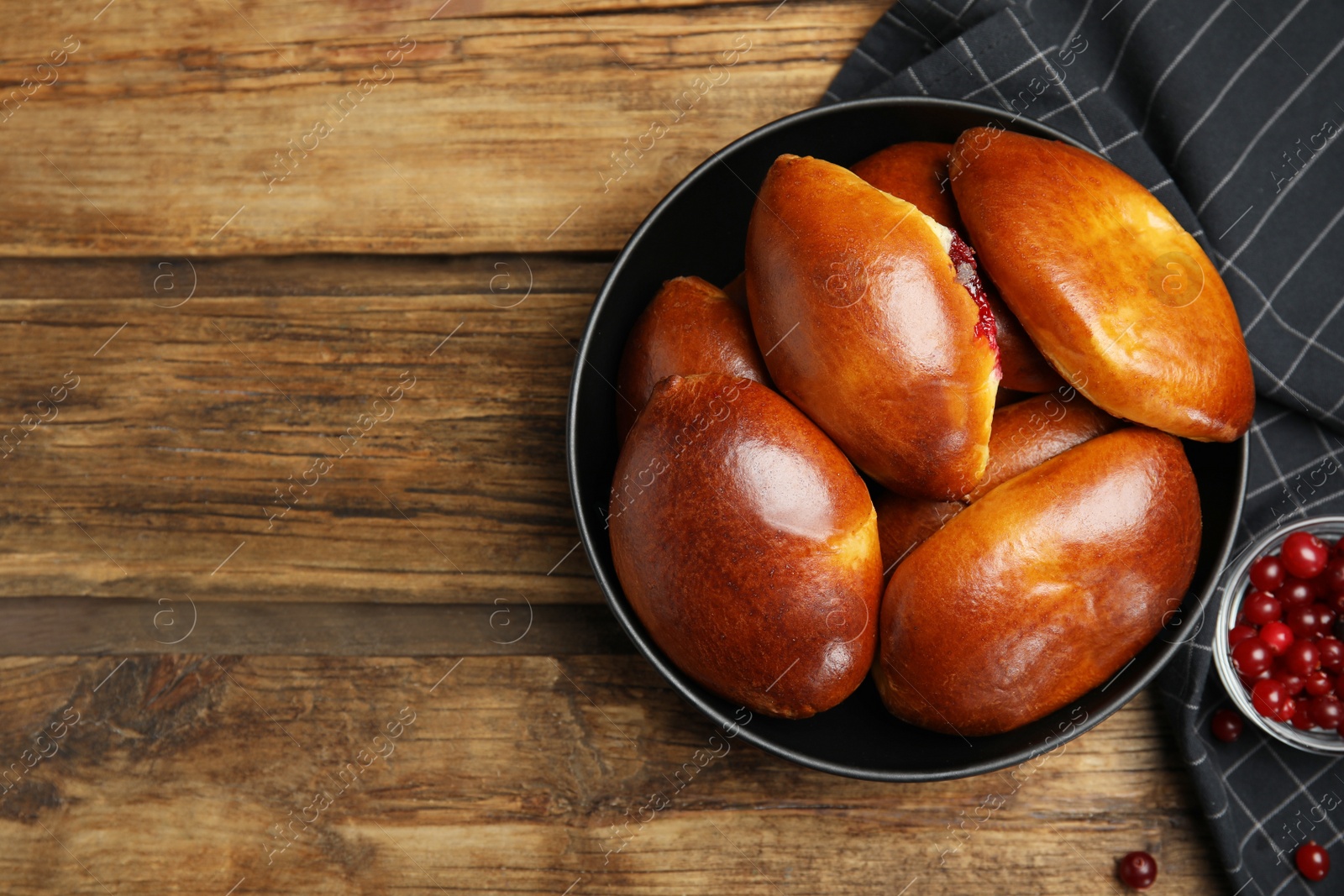 Photo of Delicious baked cranberry pirozhki in bowl on wooden table, flat lay. Space for text