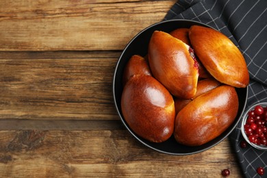 Delicious baked cranberry pirozhki in bowl on wooden table, flat lay. Space for text