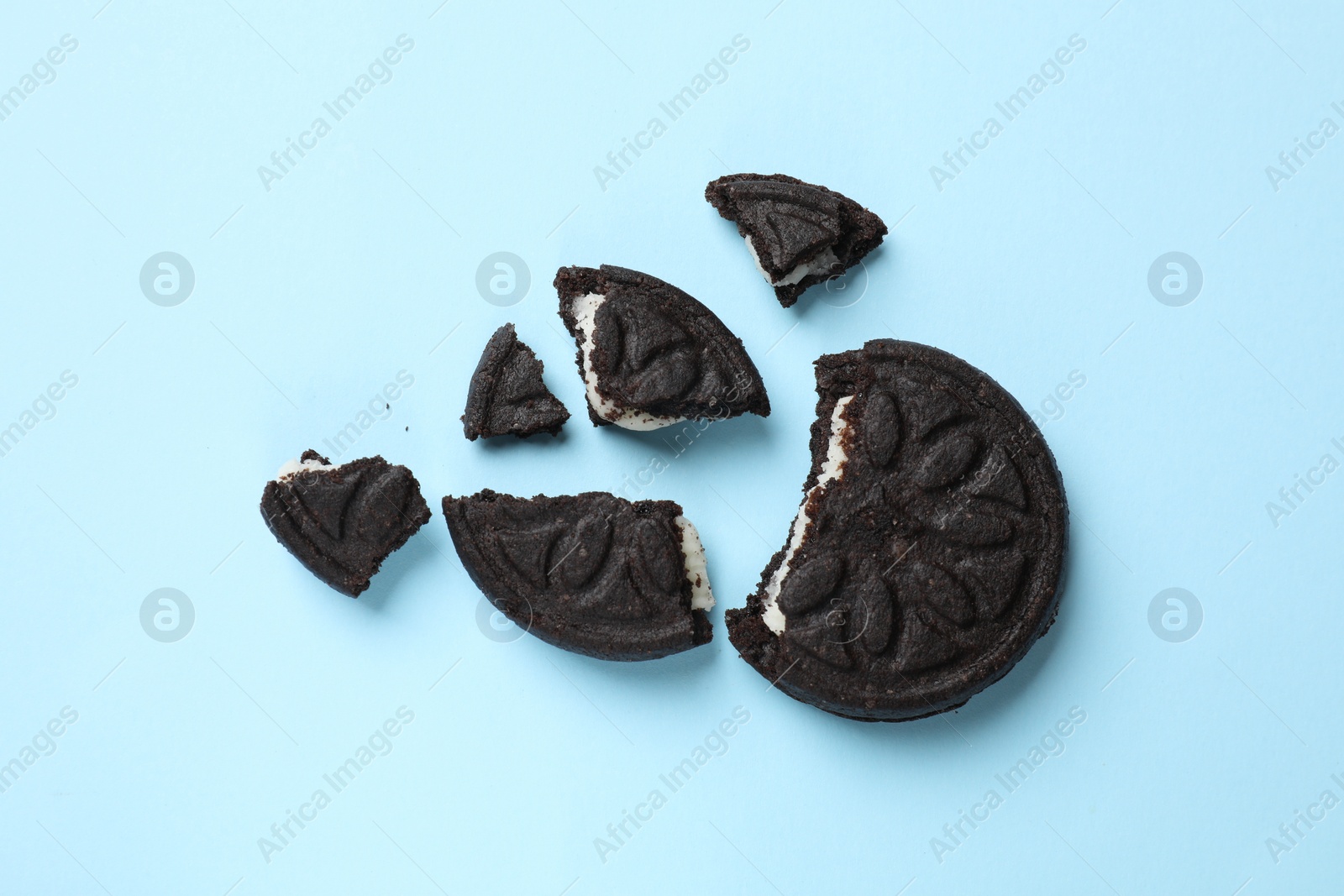 Photo of Pieces of tasty sweet sandwich cookies on light blue background, flat lay