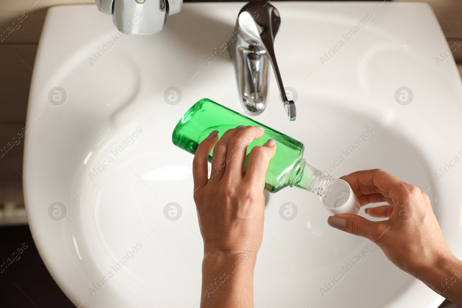 Photo of Woman pouring mouthwash from bottle into cap in bathroom, closeup. Teeth care