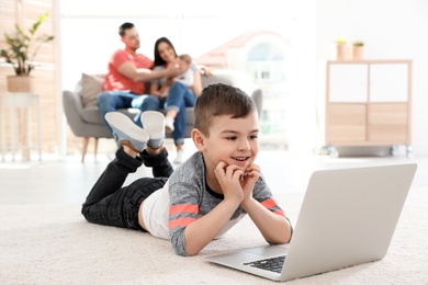 Photo of Boy with laptop lying on carpet near his family at home
