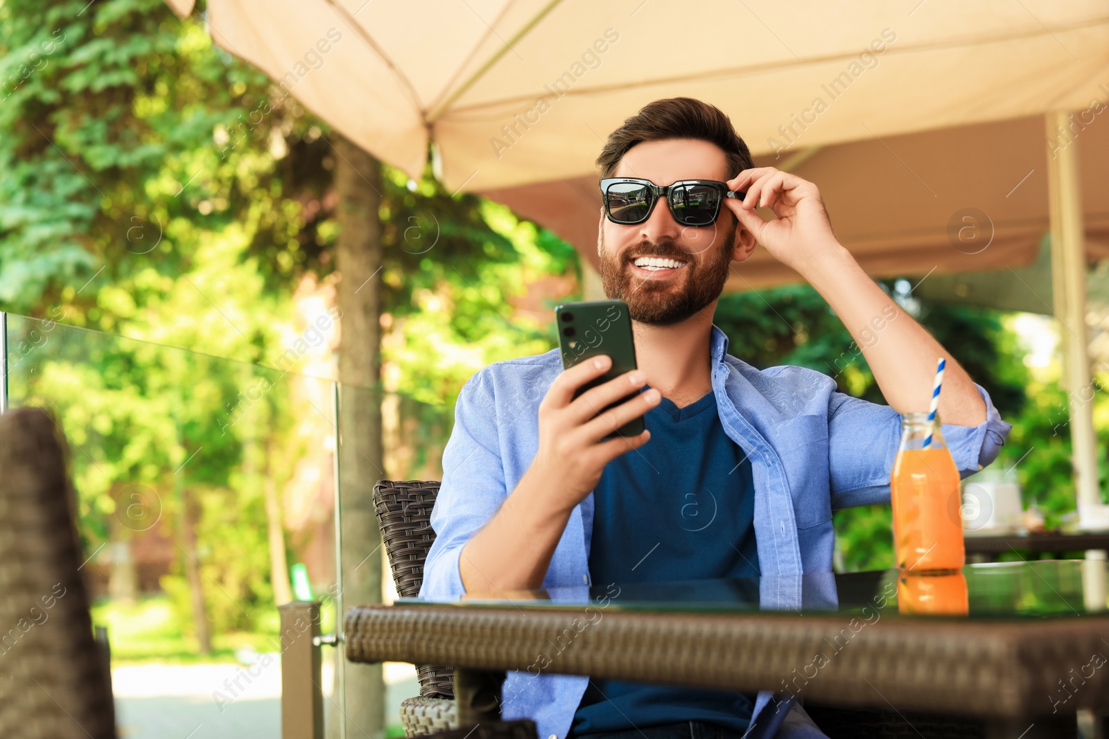 Photo of Handsome man with bottle of delicious juice in outdoor cafe. Space for text