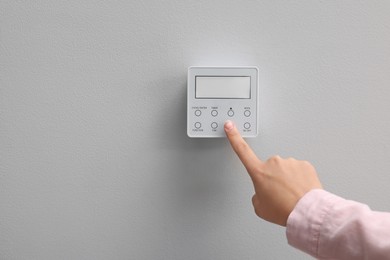 Photo of Woman adjusting thermostat on white wall, closeup and space for text. Smart home system