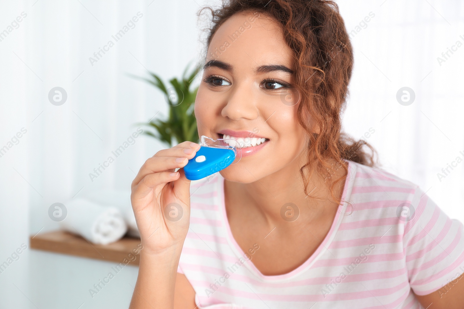 Photo of Young African-American woman using teeth whitening device at home