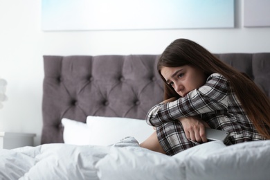 Photo of Upset teenage girl with smartphone sitting on bed. Space for text