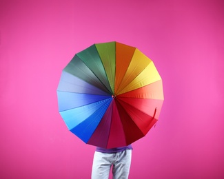 Photo of Man hiding behind rainbow umbrella on color background