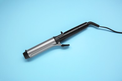 Photo of Hair styling appliance. One curling iron on light blue background, top view